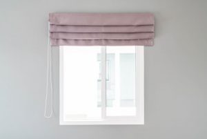 Dusty pink Roman blind raised above a white sliding window on a pale grey wall