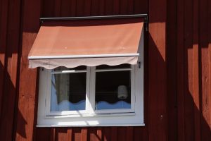 Salmon-colored fabric awning with scalloped edge over a white-framed window on a red wooden wall