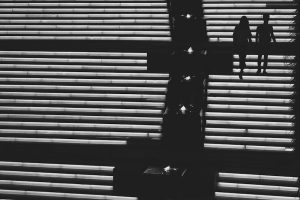 Two silhouetted people descend wide illuminated steps beside a dark central divider with small glowing lights