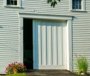 White wooden barn with horizontal siding and a vertical-plank sliding door partly open, flanked by pink flowers