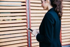 Woman in a dark blazer looks at her smartphone beside wooden slatted louvered panels with red frames