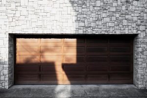 Brown wooden garage door in a white stone wall, split by sunlight and shadow