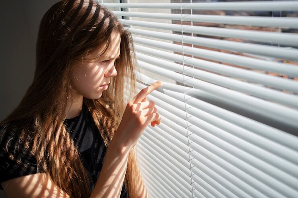 mujer joven viendo a través de persiana