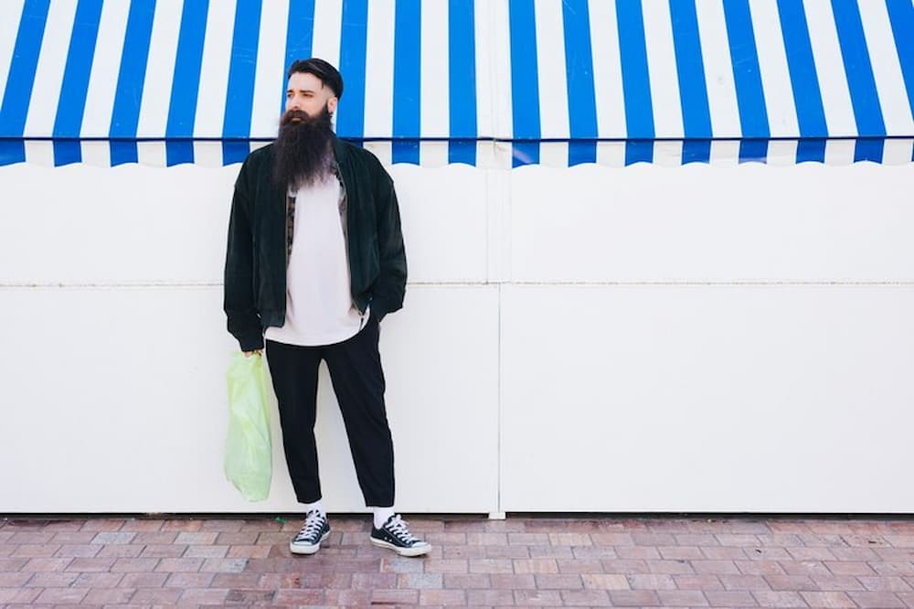 Hombre con barba de pie junto a toldo azul y blanco